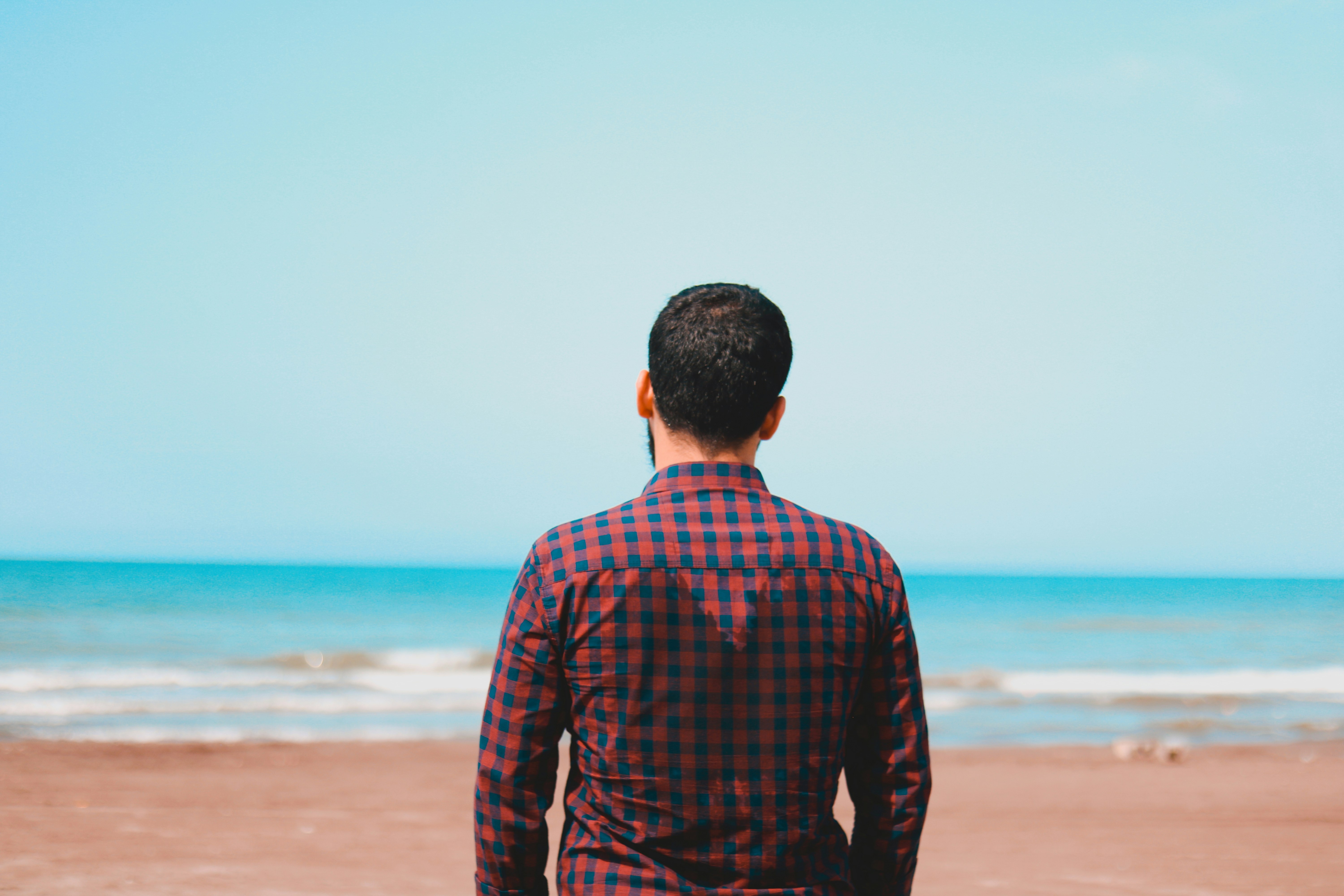 man in red and black plaid dress shirt standing on beach during daytime